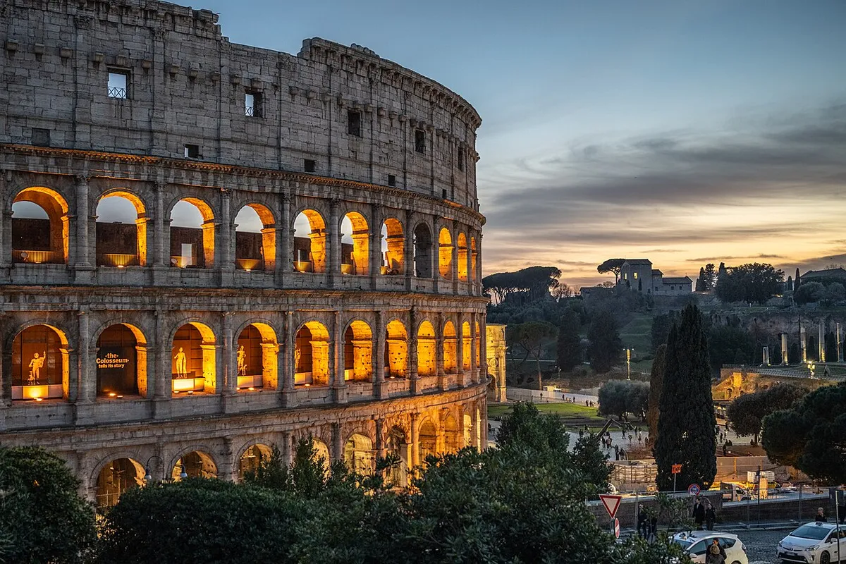 The Colosseum lit up at dusk, with the Palatine Hill in the background